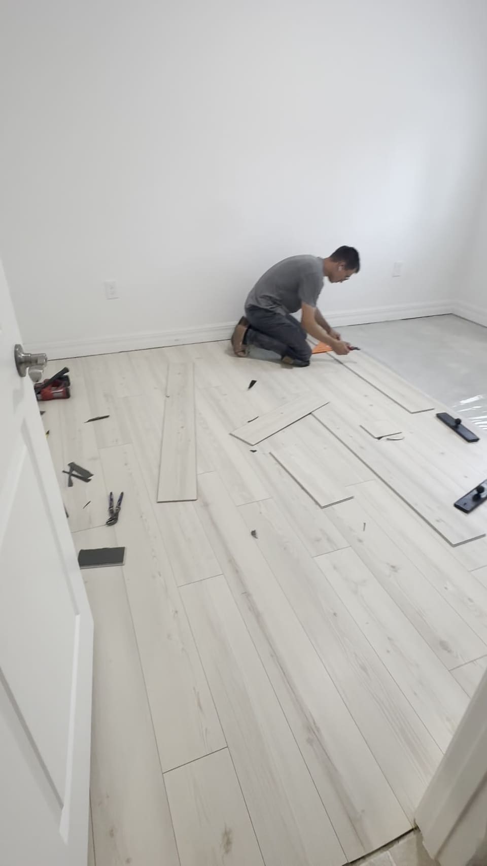 Flooring installer laying light wood look plank in a bedroom