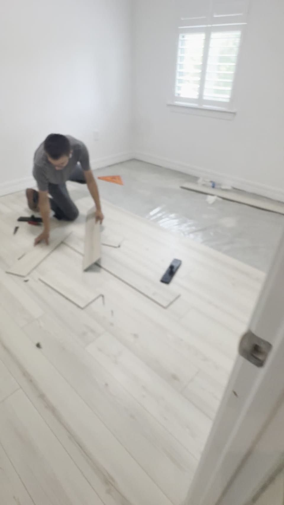 Installer laying plank flooring across an empty bedroom